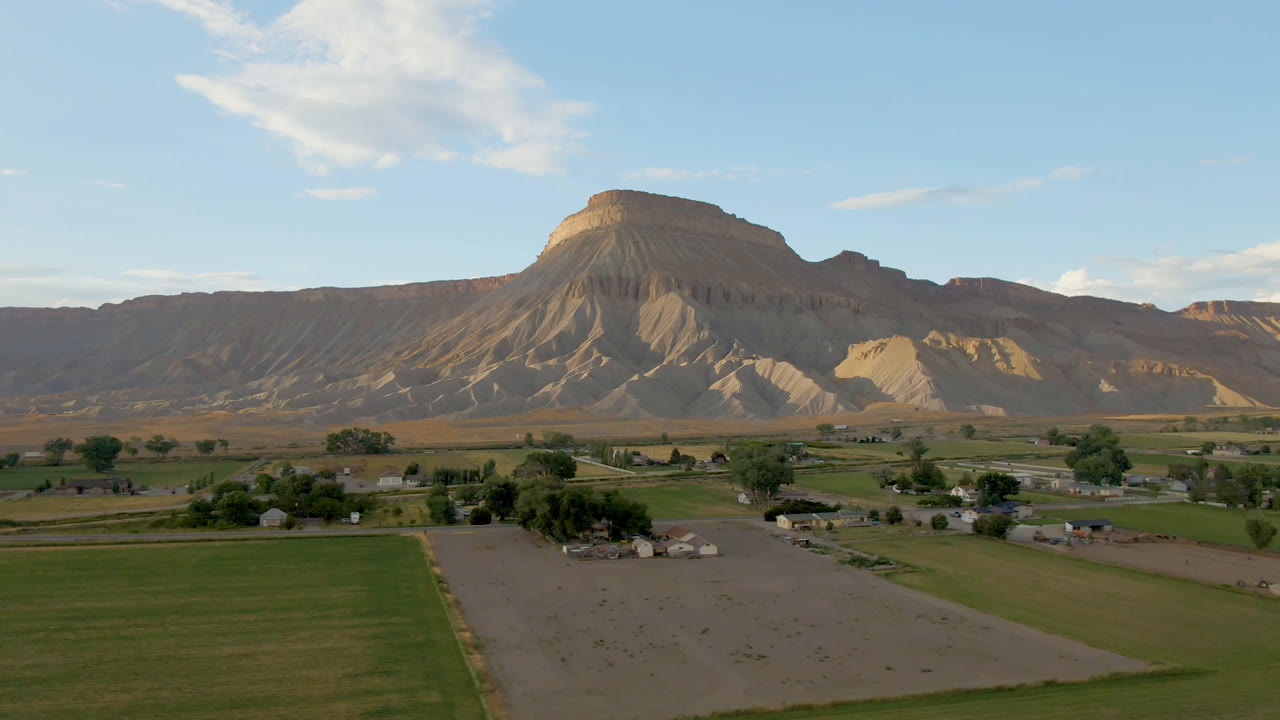 Second frame shows the Palisades, Colorado rural edge from above, with a darker green field in front, low buildings near trees, the mesa ridge behind, and no visible people.