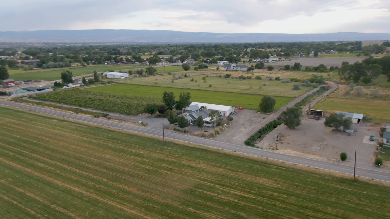 Aerial view in Palisades, Colorado, showing the road running across the lower frame, a green field block behind it, a farmhouse cluster, trees, low hills, and no visible people.