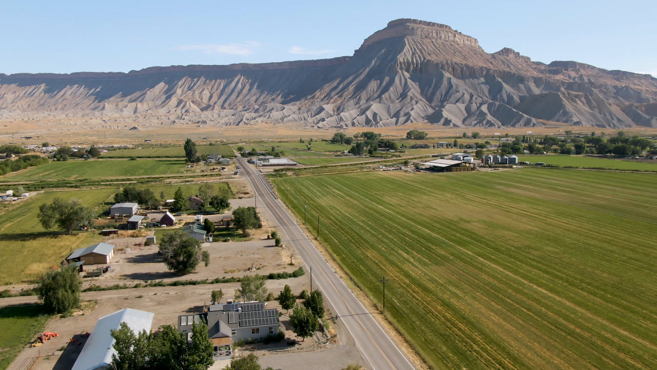 Aerial view of green farm fields, a road, scattered buildings, and a mesa.