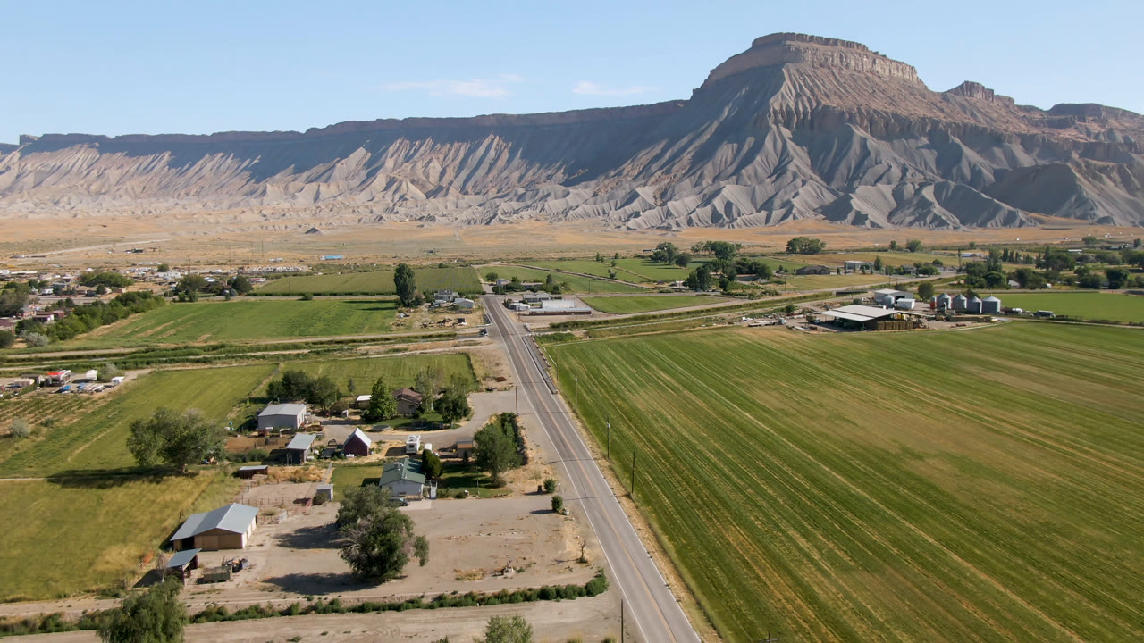 Aerial view of green fields, a paved road, farm buildings, and a mountain ridge.