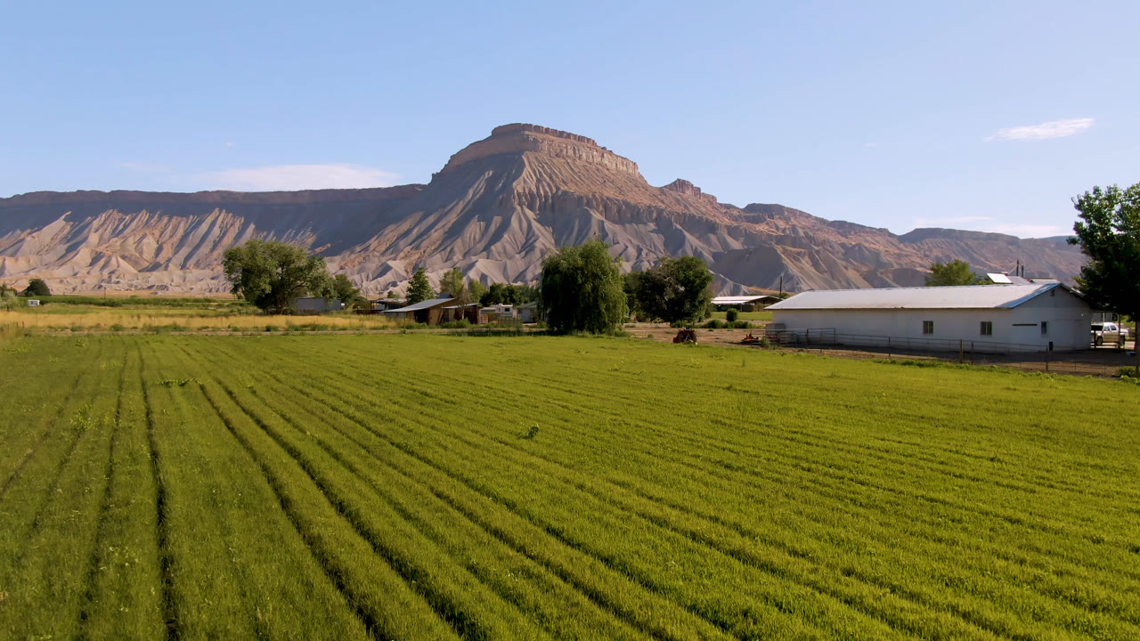 Green field rows with farm buildings, trees, and a tan mountain ridge beyond.