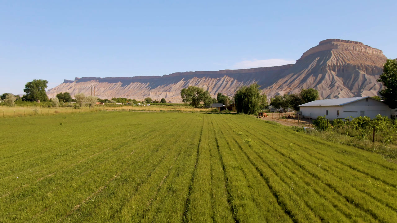 Wide rural field with white house at right and mountain ridge behind.