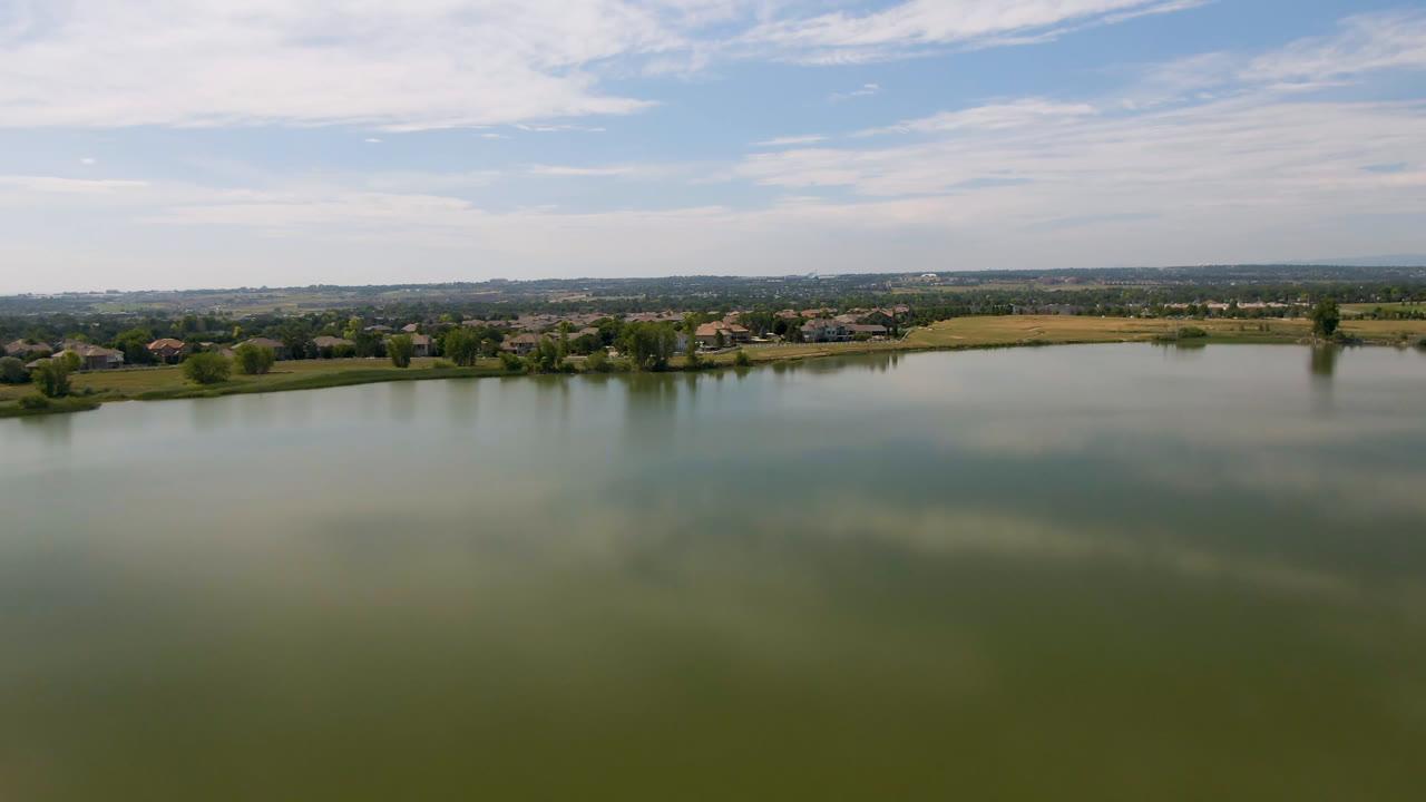 Second frame shows the Broomfield lake surface occupying most of the foreground, with a thin band of shoreline, fields, distant buildings, and no visible people.