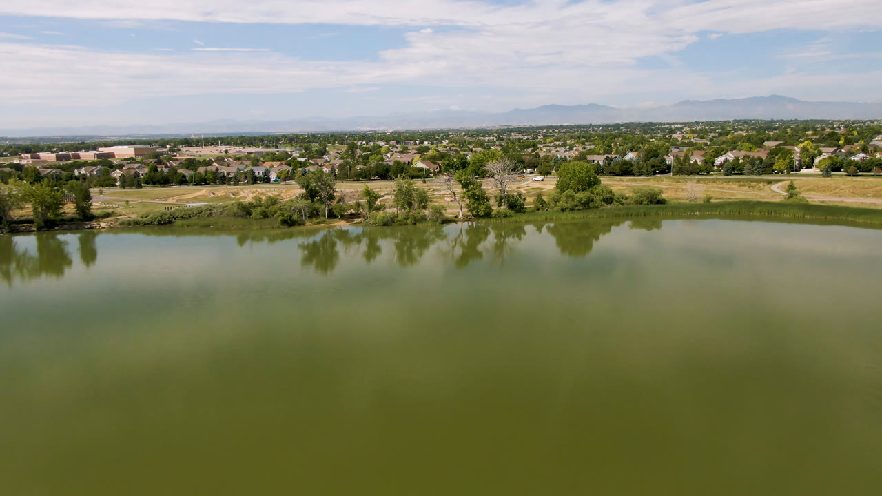 Aerial view of green lake water with shoreline trees and a town beyond.
