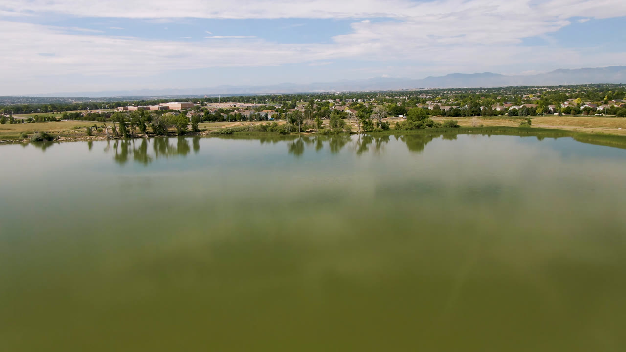Wide lake view with distant town, trees, clouds, and faint mountains