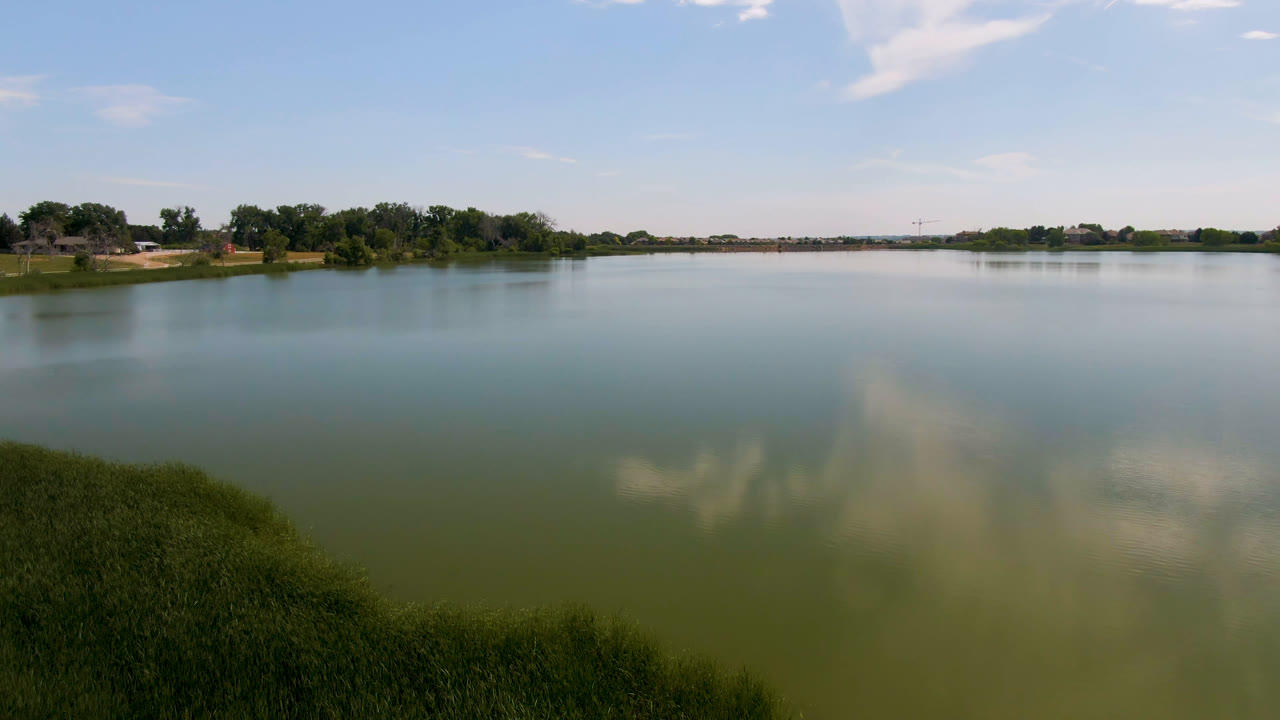 Wide lake with grass in the foreground and trees across the water.