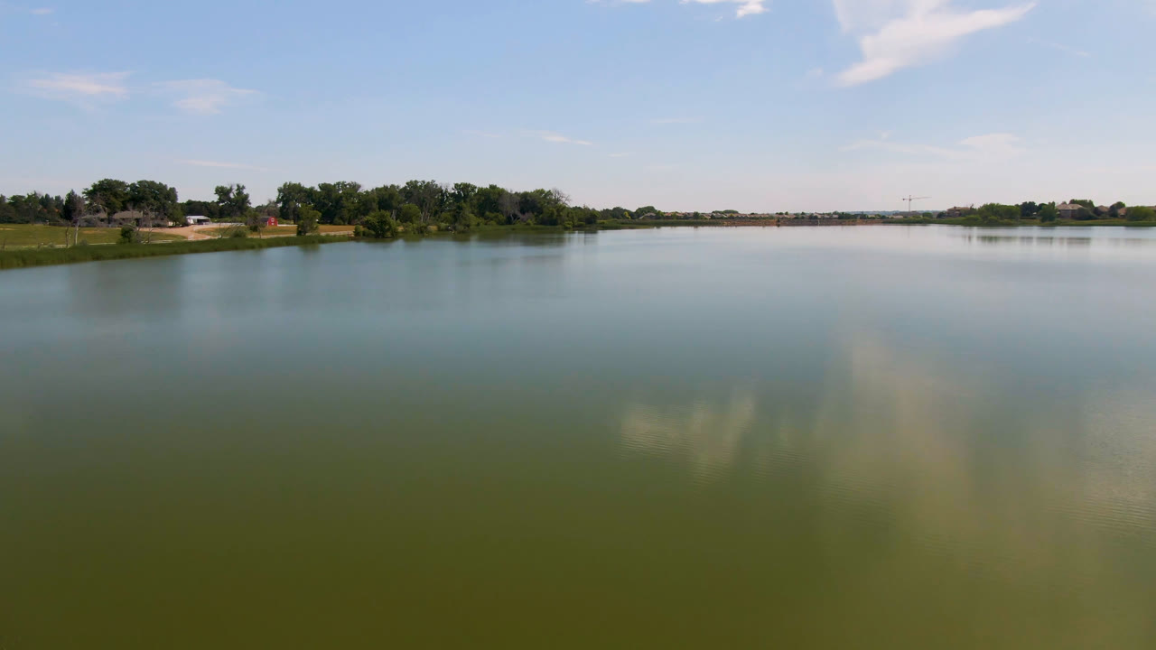 Broomfield, Colorado lake scene with the water stretching across the frame, a low tree-lined shore in the distance, a grassy edge at left, and no visible people.