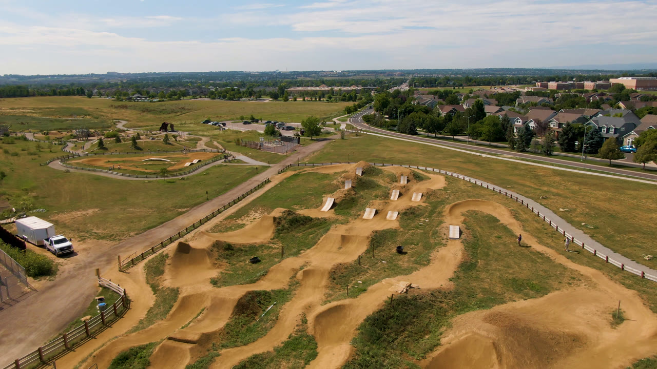 Drone wide shot of tan dirt track features with fields and houses beyond.