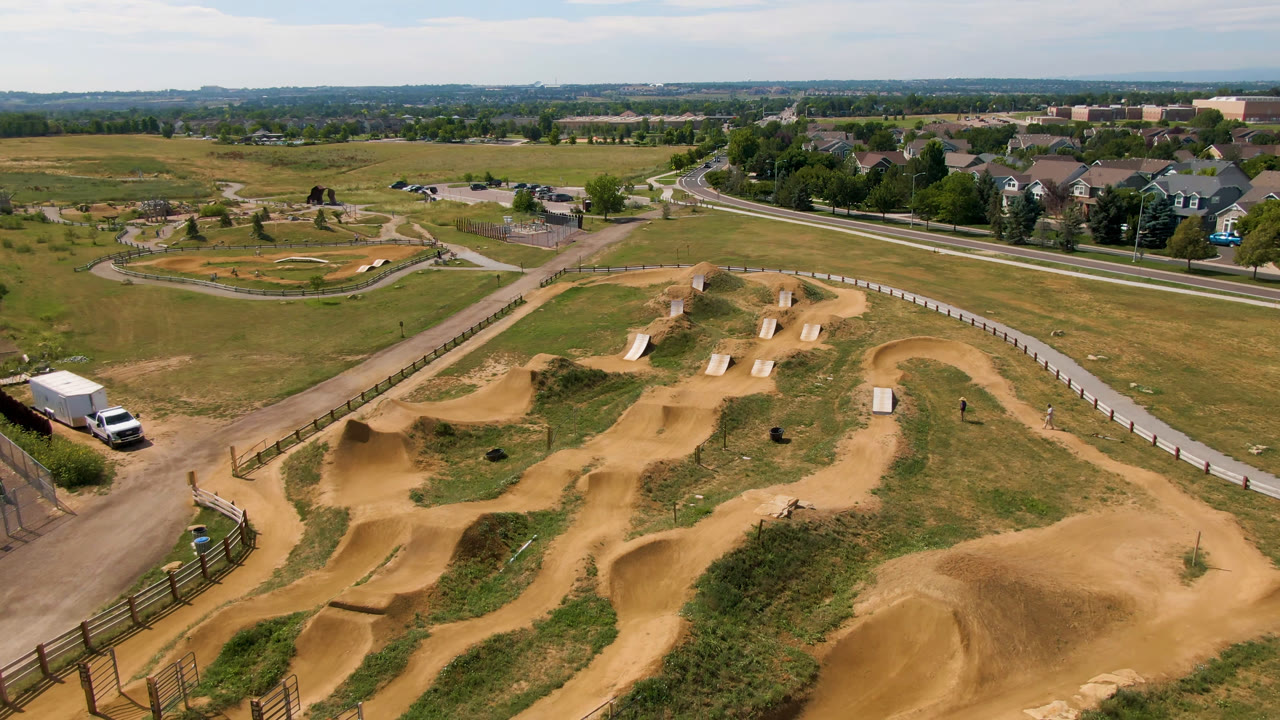Drone view of tan dirt bike tracks in open grass beside roads and houses.