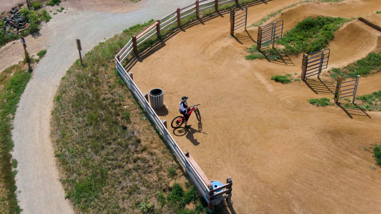 Overhead view of a BMX rider beside a fence on a dirt course.