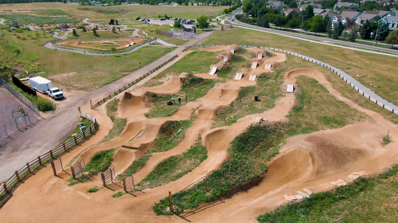 High-angle view of tan dirt track curves, fence lines, grass, and a small white structure.