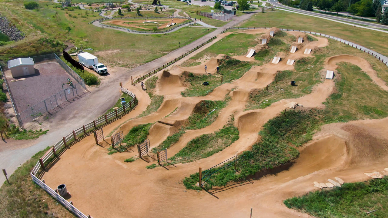 Aerial view of dirt jumps, paths, fencing, grass, and a paved area.