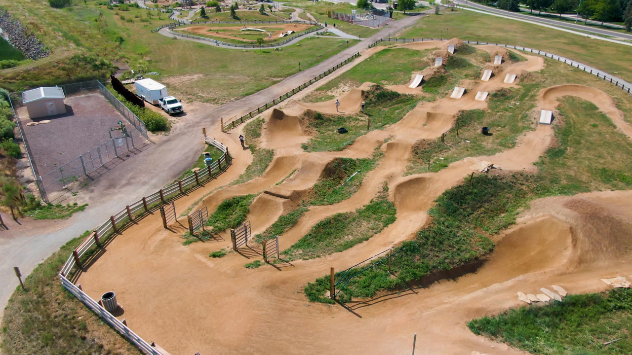 Third frame of the Broomfield overhead shot, with tan berms and winding dirt tracks across green grass, plus roads, small buildings, and no visible people.
