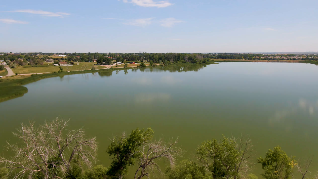 Large lake with treetops in front and low buildings beyond the shoreline.