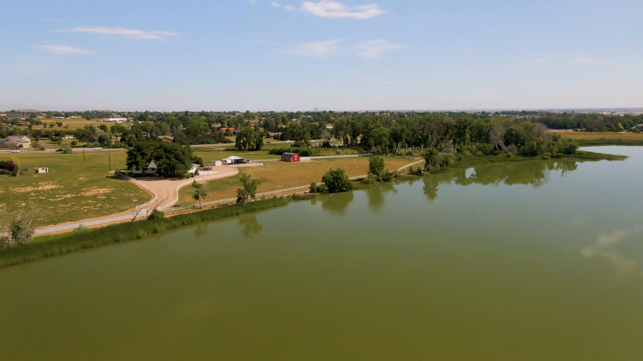 Aerial view over green water, fields, a curving road, trees, and distant buildings.