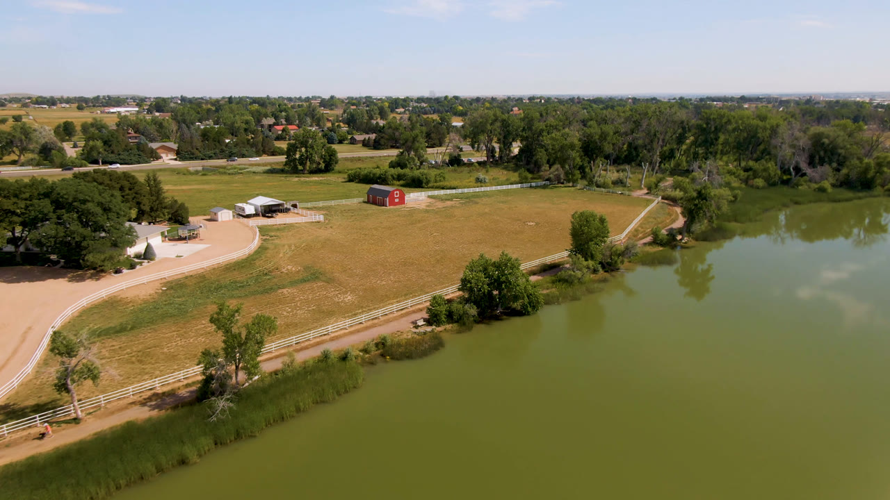 Aerial farmland scene with pond, fence, road, trees, and barn.