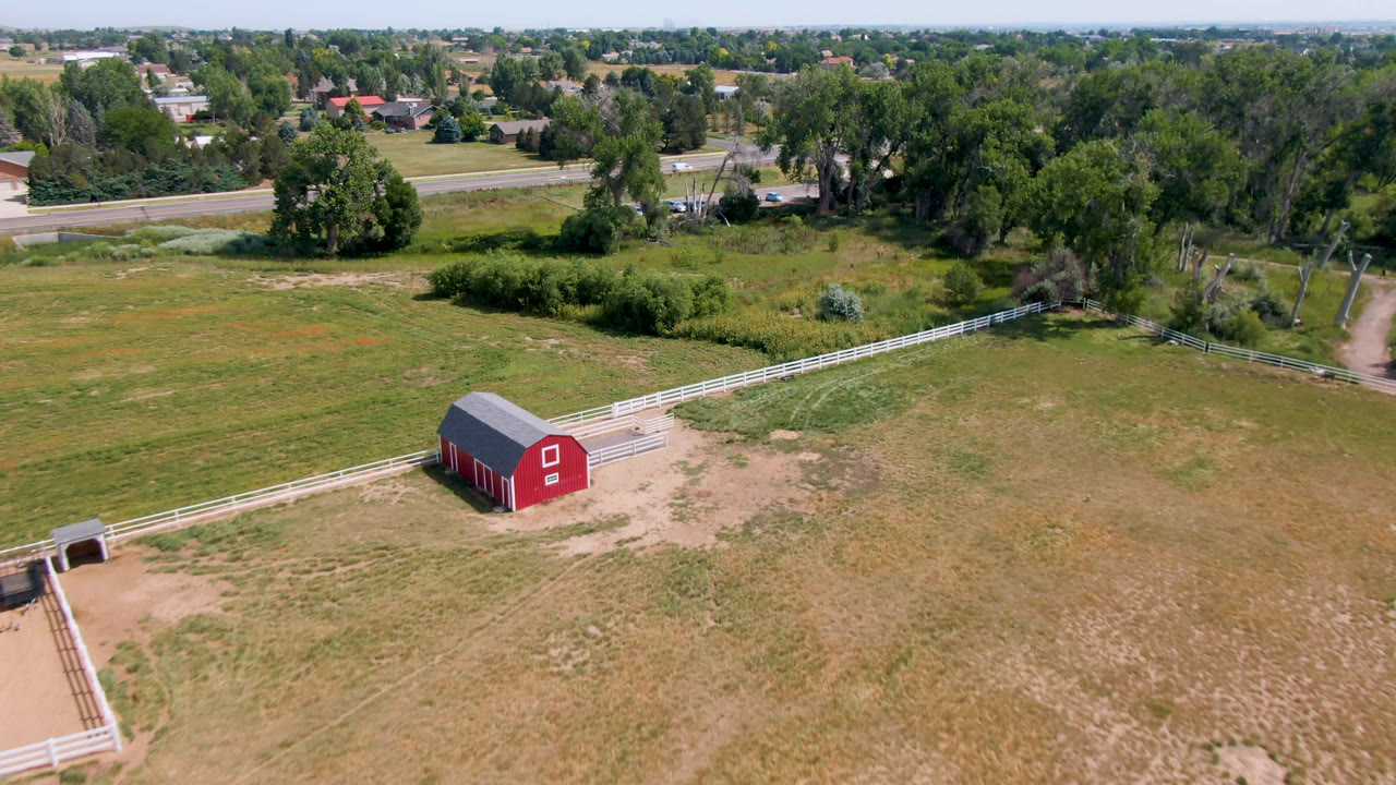 Aerial view of a red barn in a grassy field near a road and trees.