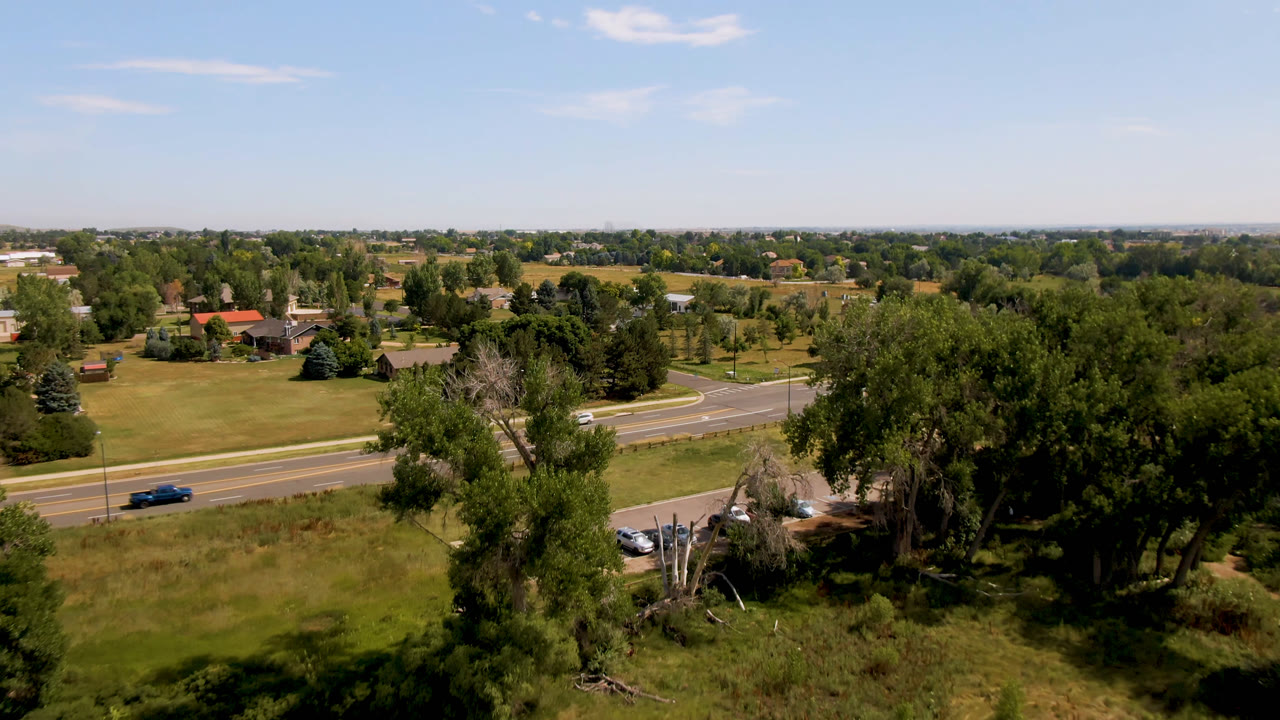 Aerial roadside scene with a blue car, trees, grass, and distant houses.