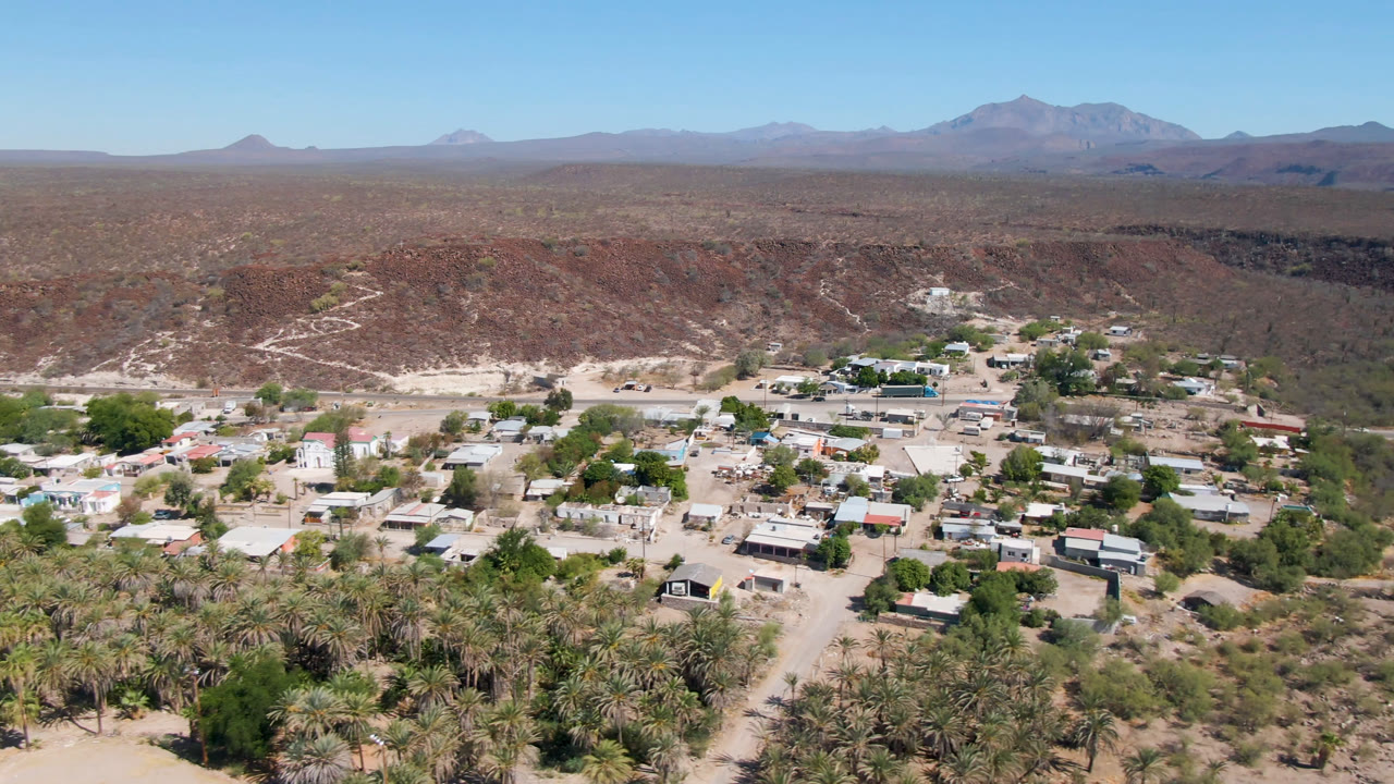 Aerial view of a small desert town below a rocky ridge and distant mountains.