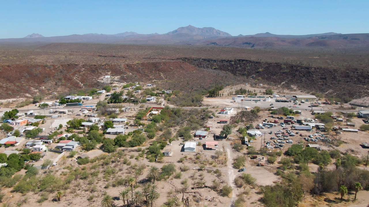 Wide aerial view of a desert town with roads, trees, and distant mountains.
