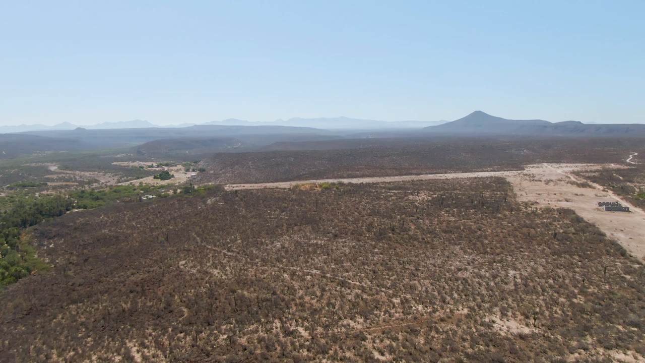 High aerial view of brown desert, winding dirt track, green vegetation, and hazy mountains.