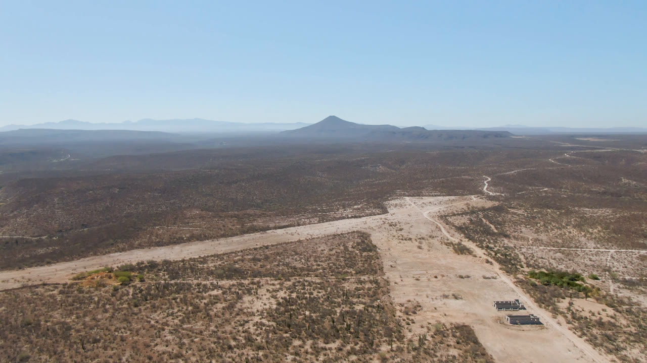 High desert aerial with crossing dirt tracks, scrubland, dry wash, distant mountains, and clear sky.