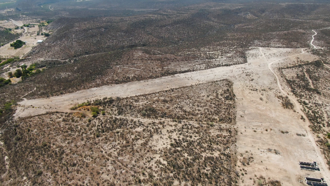 High aerial frame over San Ignacio, Baja California Sur, showing a pale dirt road and dry wash cutting through scrub desert, with no visible people.