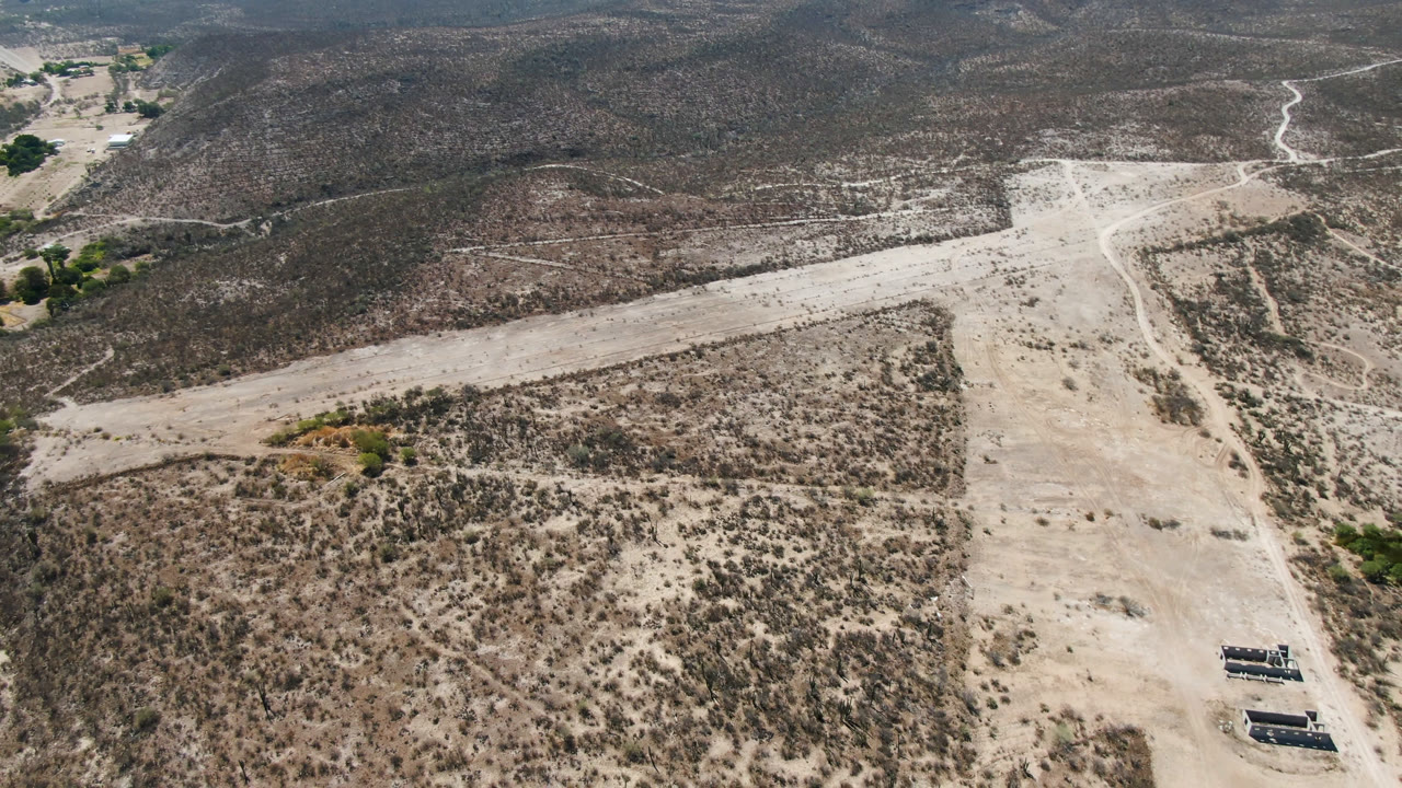 Wide drone view of desert scrub and a dirt road beside low ridges.