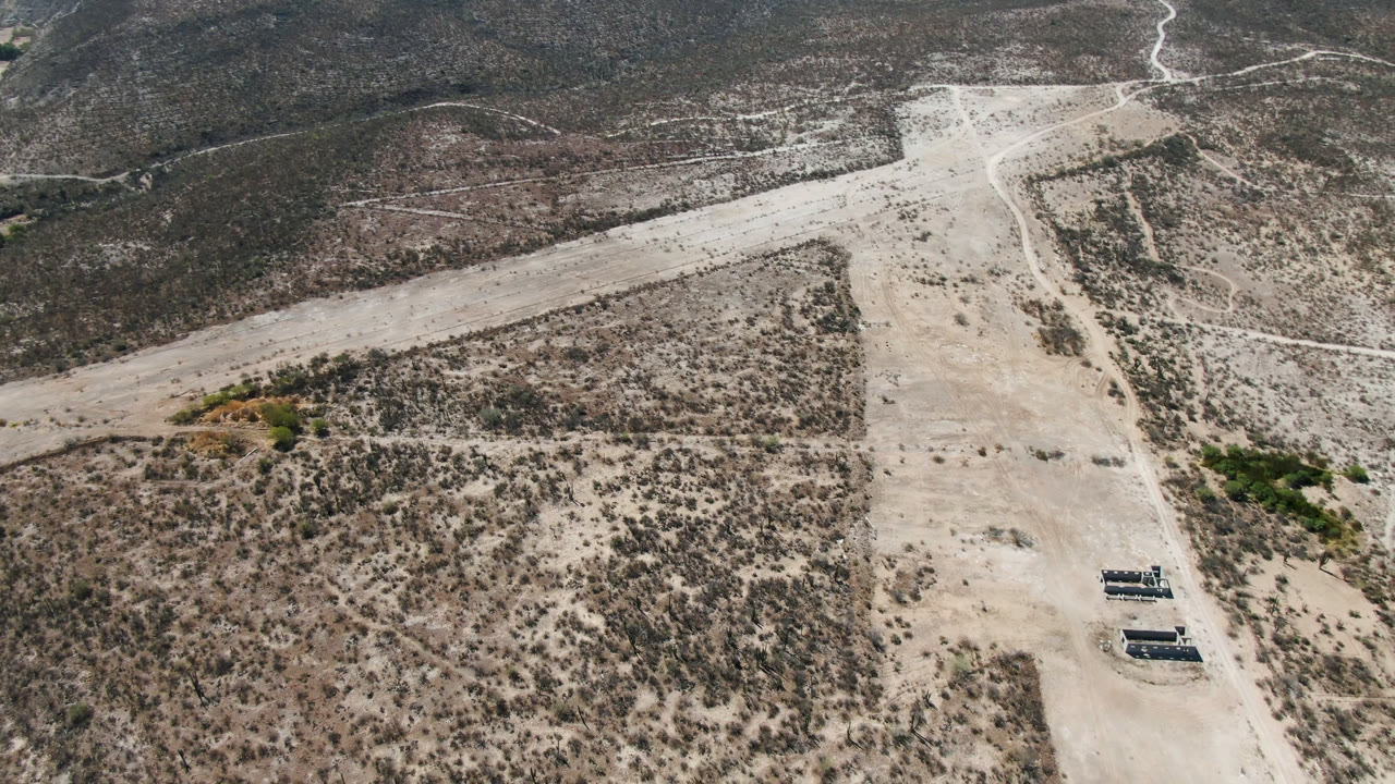 Aerial frame over San Ignacio, Baja California Sur, Mexico showing a pale dirt road crossing scrub desert with low hills beyond and no visible people.