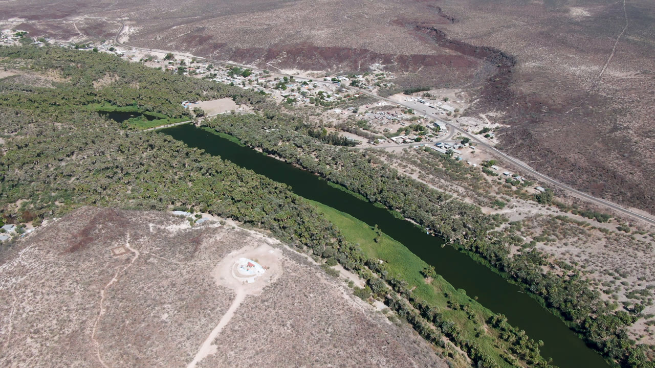 Aerial view of a green river running through dry hills and trees.