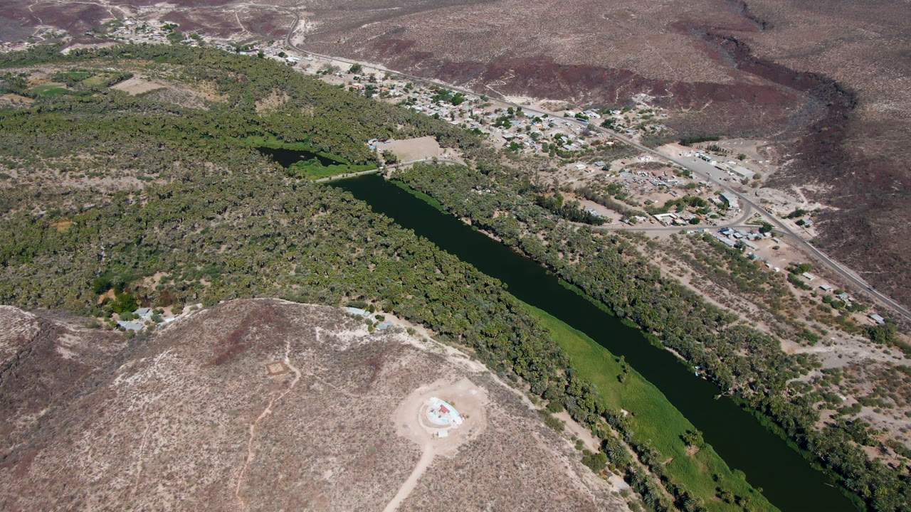 Aerial view of a green river through palms and dry hills