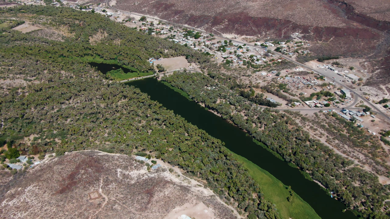 Aerial view of a green river through trees beside dry hills and roads