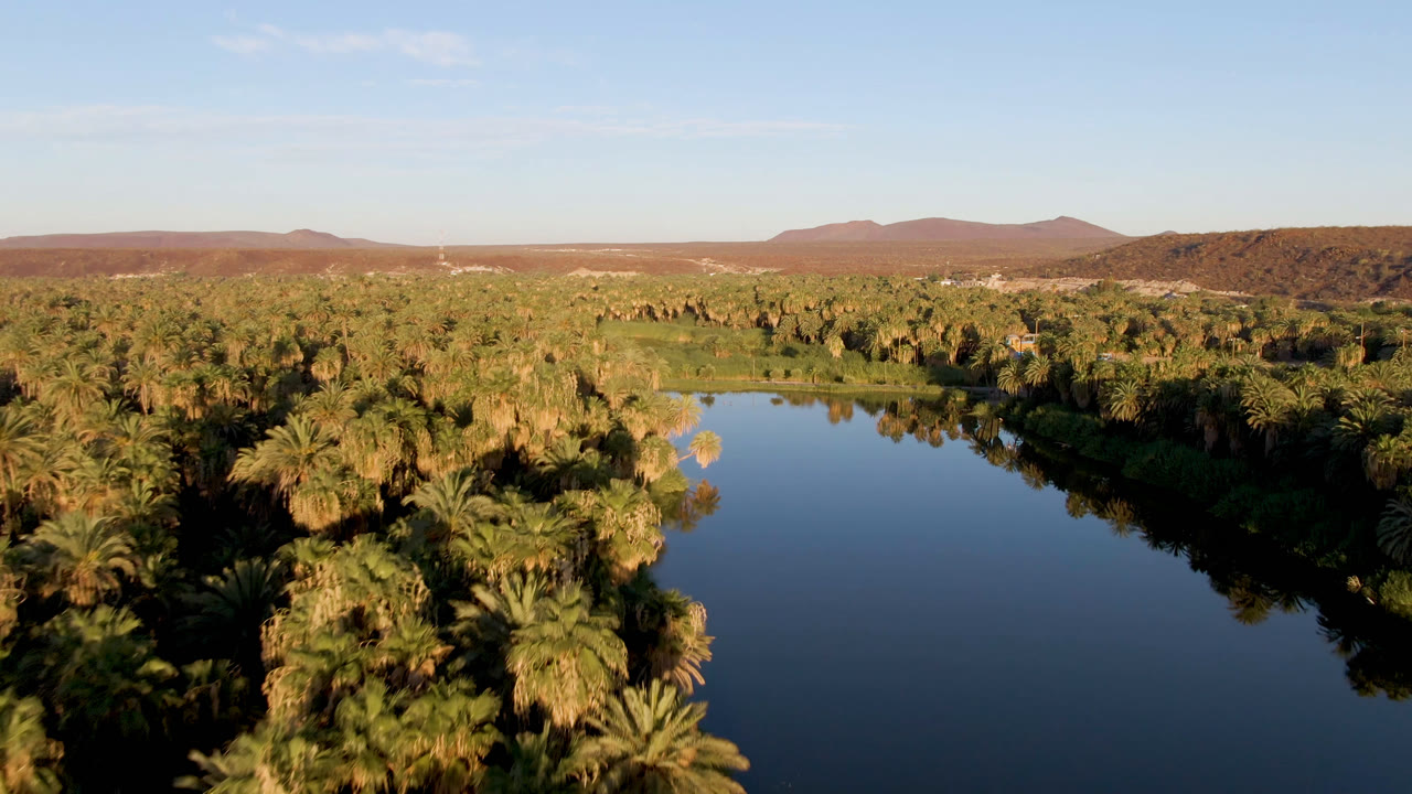 Wide aerial landscape of a river bend surrounded by palms and desert mountains.