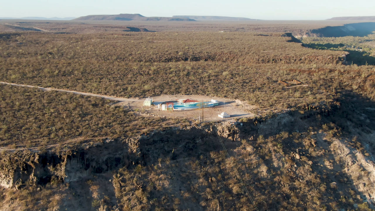 Drone view of a desert building compound near a rocky canyon rim.
