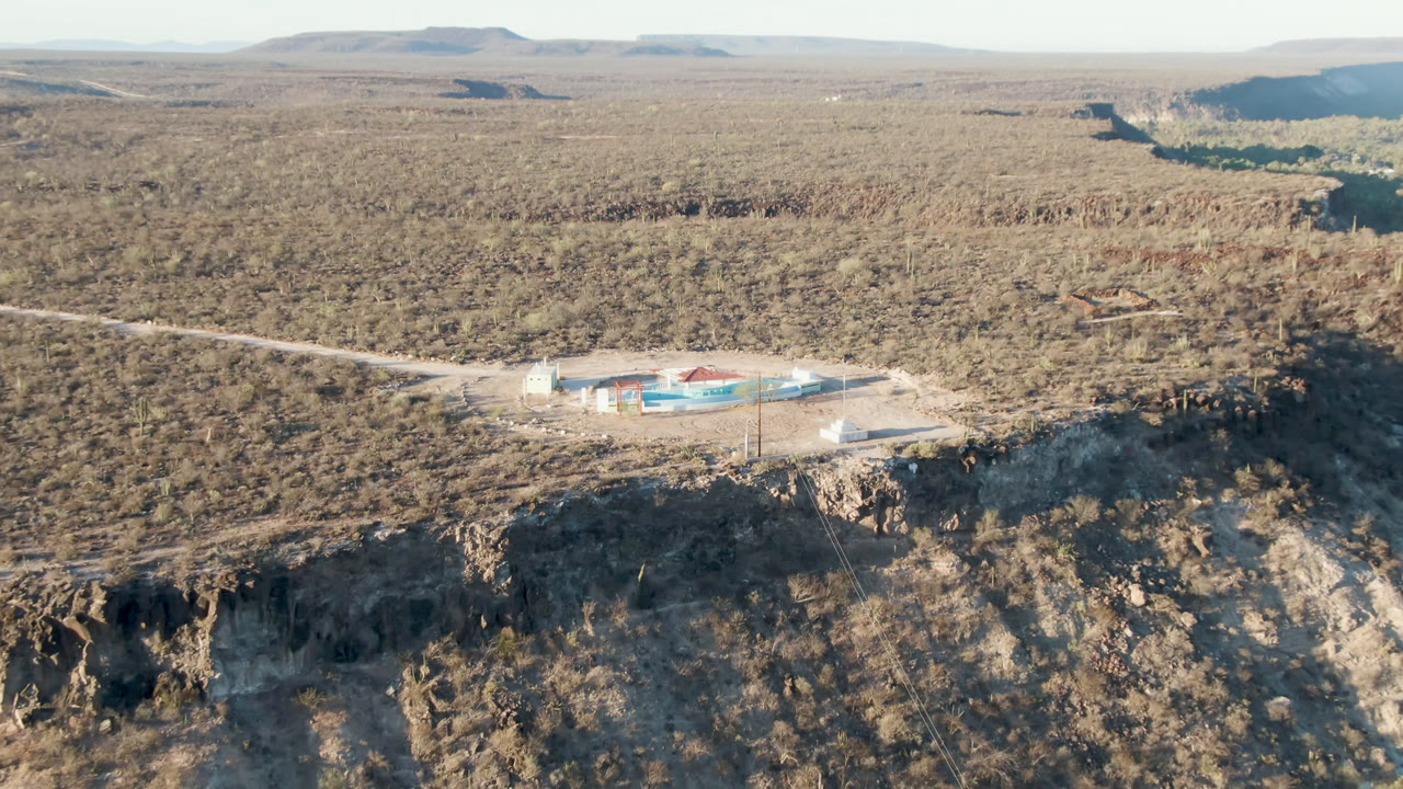 High aerial view of a large building near a road on a desert cliff with mesas beyond.