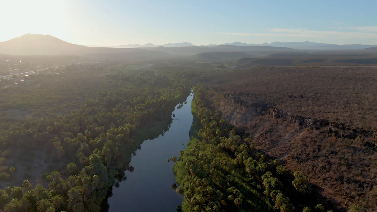 Wide aerial landscape with river, trees, desert scrub, and mountains