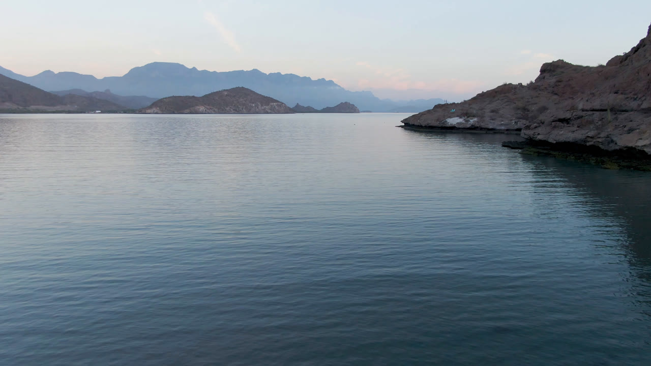 Wide view of calm water, rocky islands, and hazy mountains in Loreto, Mexico, with no visible people at the start of the clip.