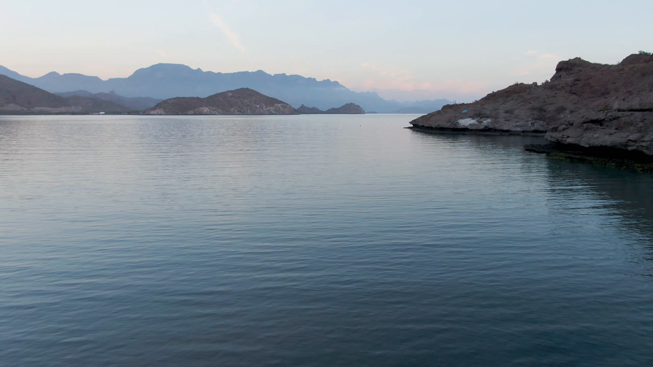 Dark rocky island beside still water and distant mountains