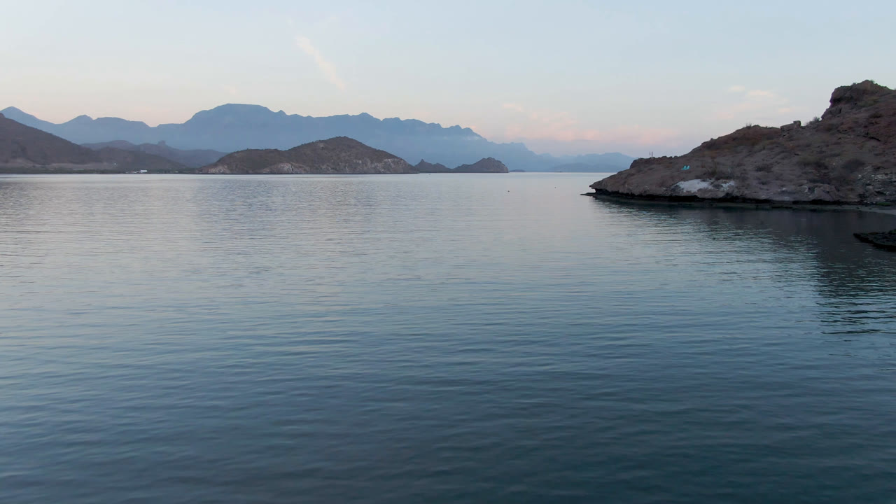 Calm Loreto, Mexico coastal water stretches across the foreground as the rocky island sits near the center-right with darker reflections and no visible people.