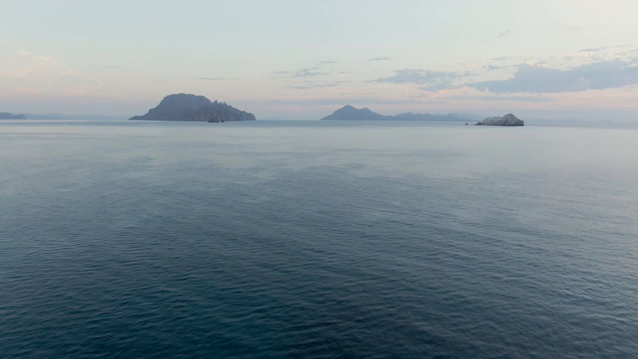 Wide view of Danzante Bay in Loreto, Baja California Sur, with blue-gray water in the foreground, dark islands on the horizon, soft cloud cover, and no visible people.