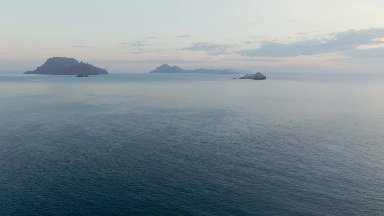 Wide aerial view over Danzante Bay near Loreto, Mexico, with blue-green water, dark islands on the horizon, pale clouds, and no visible people.