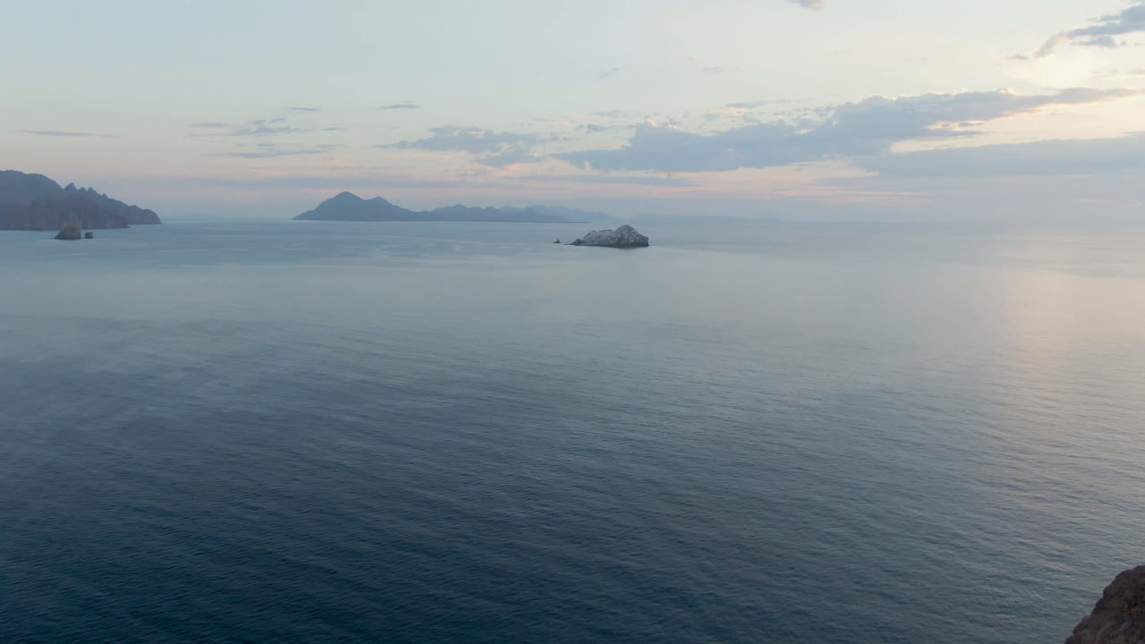 Opening frame of Danzante Bay in Loreto, Baja California Sur, with calm water in the foreground, small islands on the horizon, pale clouds overhead, and no visible people.