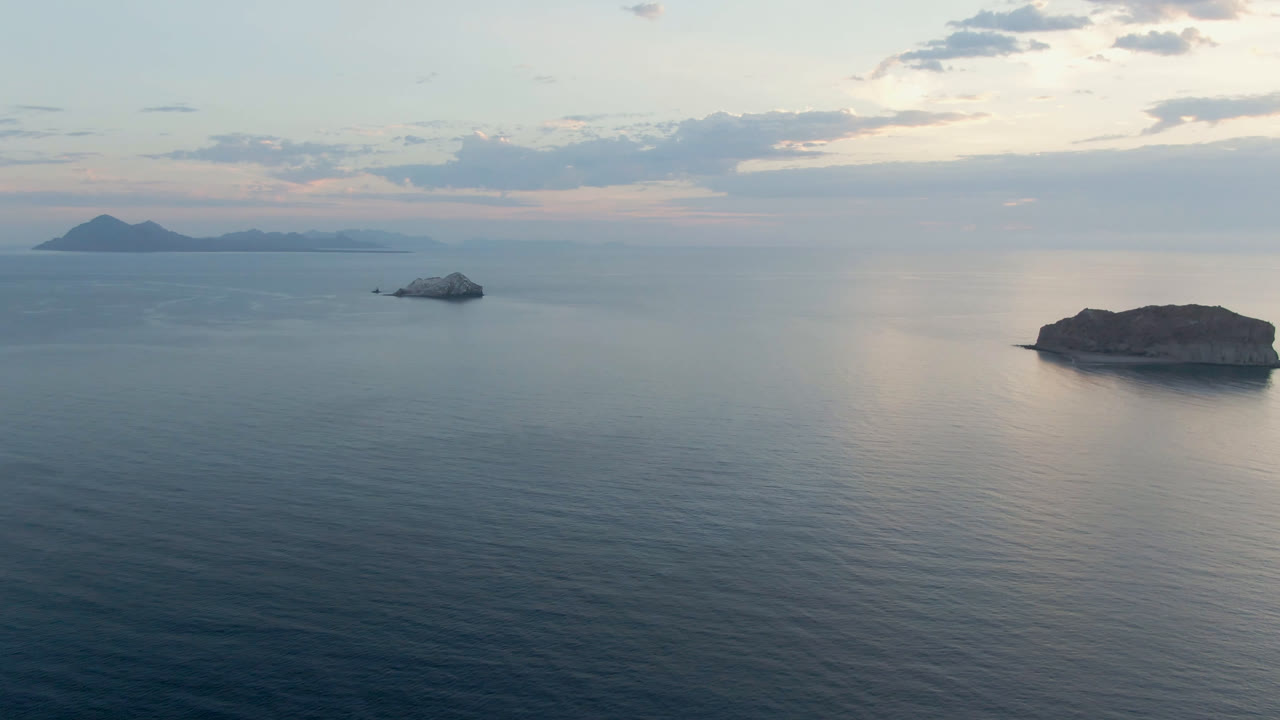 Opening frame of Danzante Bay, Loreto with calm blue water, two small boats near a low island, distant island silhouettes on the horizon, and no visible people.