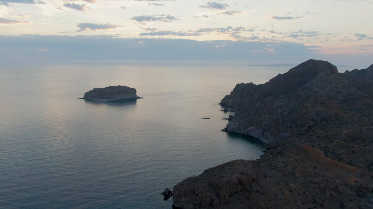 Aerial view over Danzante Bay Loreto with a small boat on calm water near a rocky shoreline, an offshore island to the left, dark hills to the right, and no visible people.