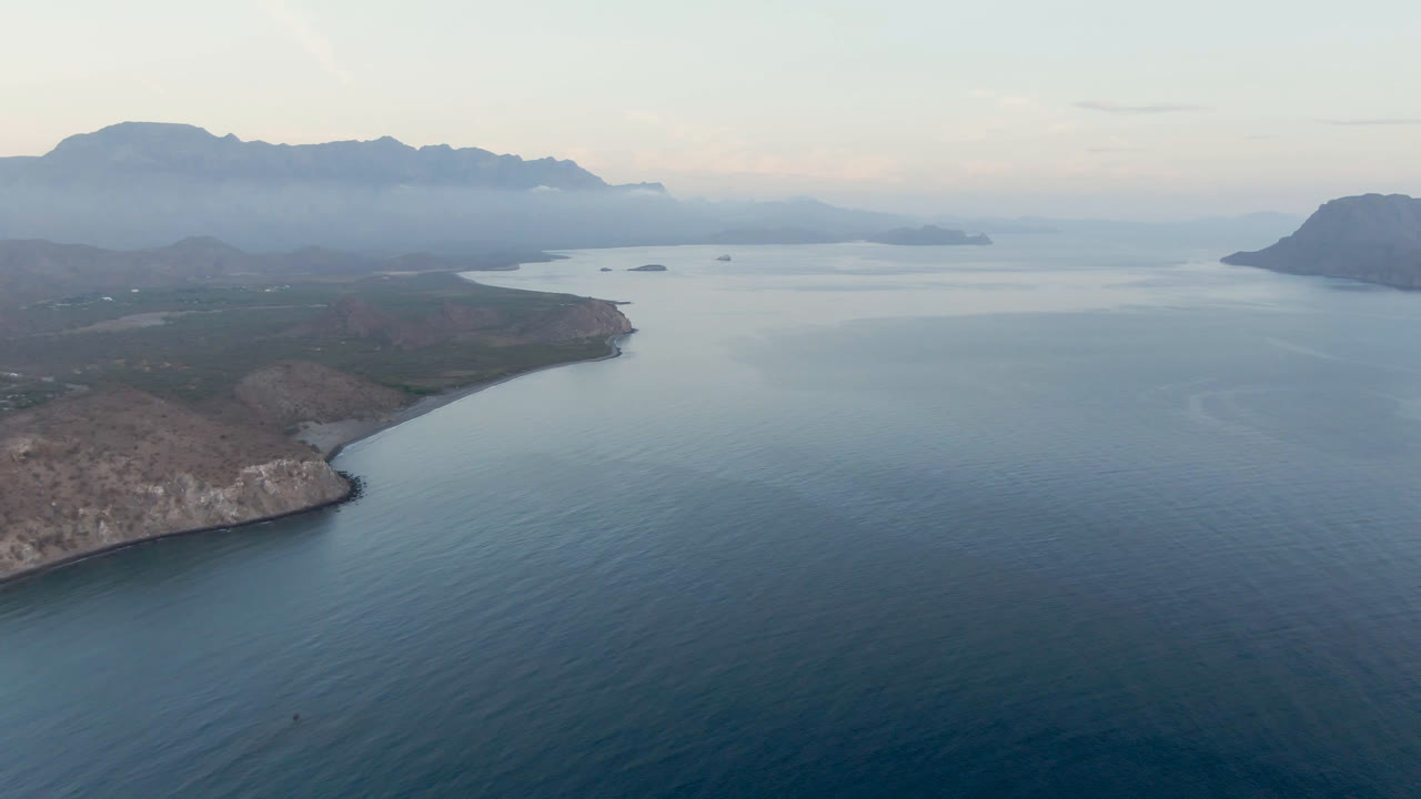 Elevated view across calm water toward a rocky peninsula and mountain horizon.