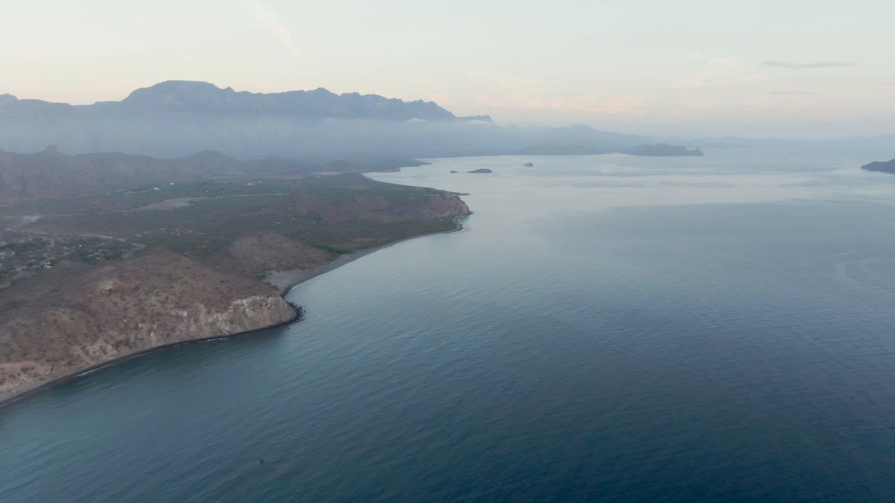 Aerial view of blue bay water, rocky coast, and distant mountains.