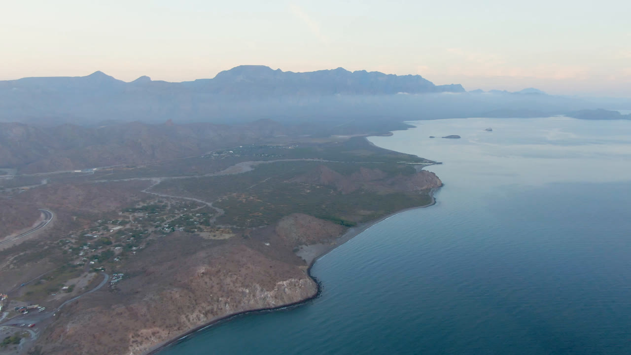 Aerial view of bay water, rocky shore, small town, and distant mountains.