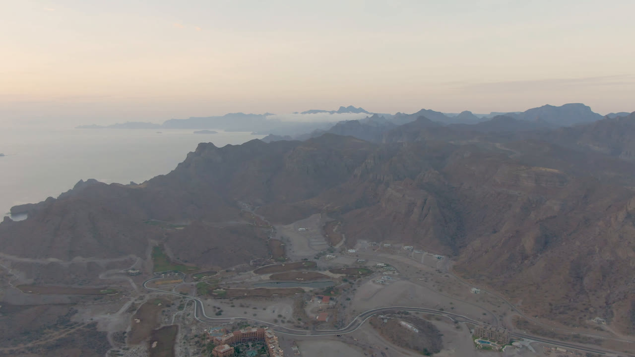 Opening aerial frame over Danzante Bay, Loreto, Baja California Sur, with rocky mountains, a road grid, calm water, distant islands, and no visible people.