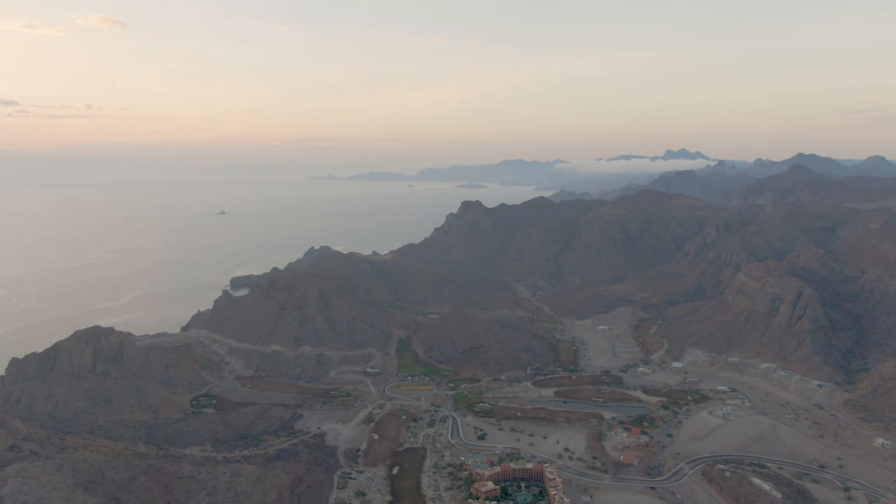 Wide aerial frame over Danzante Bay Loreto, Baja California Sur, showing rugged mountain ridges, coastal roads, ocean horizon, distant islands, and no visible people.