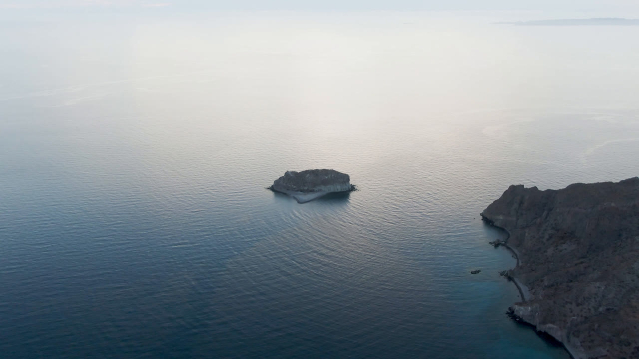 Aerial view of calm ocean with a small rocky islet and a larger island edge.